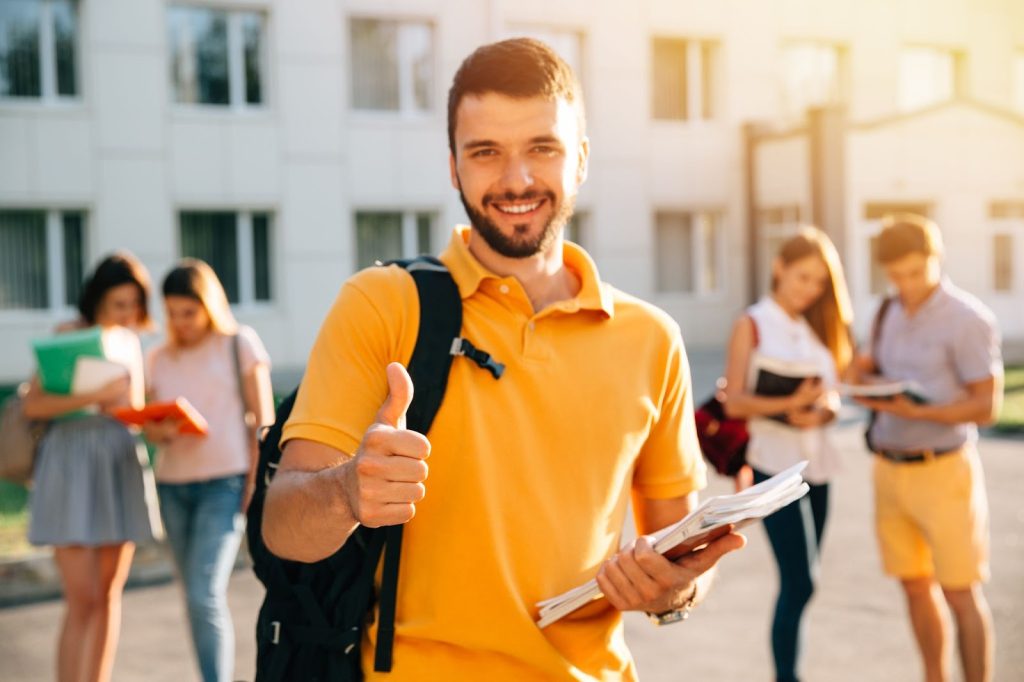 young attractive smiling student showing thumb up outdoors campus university